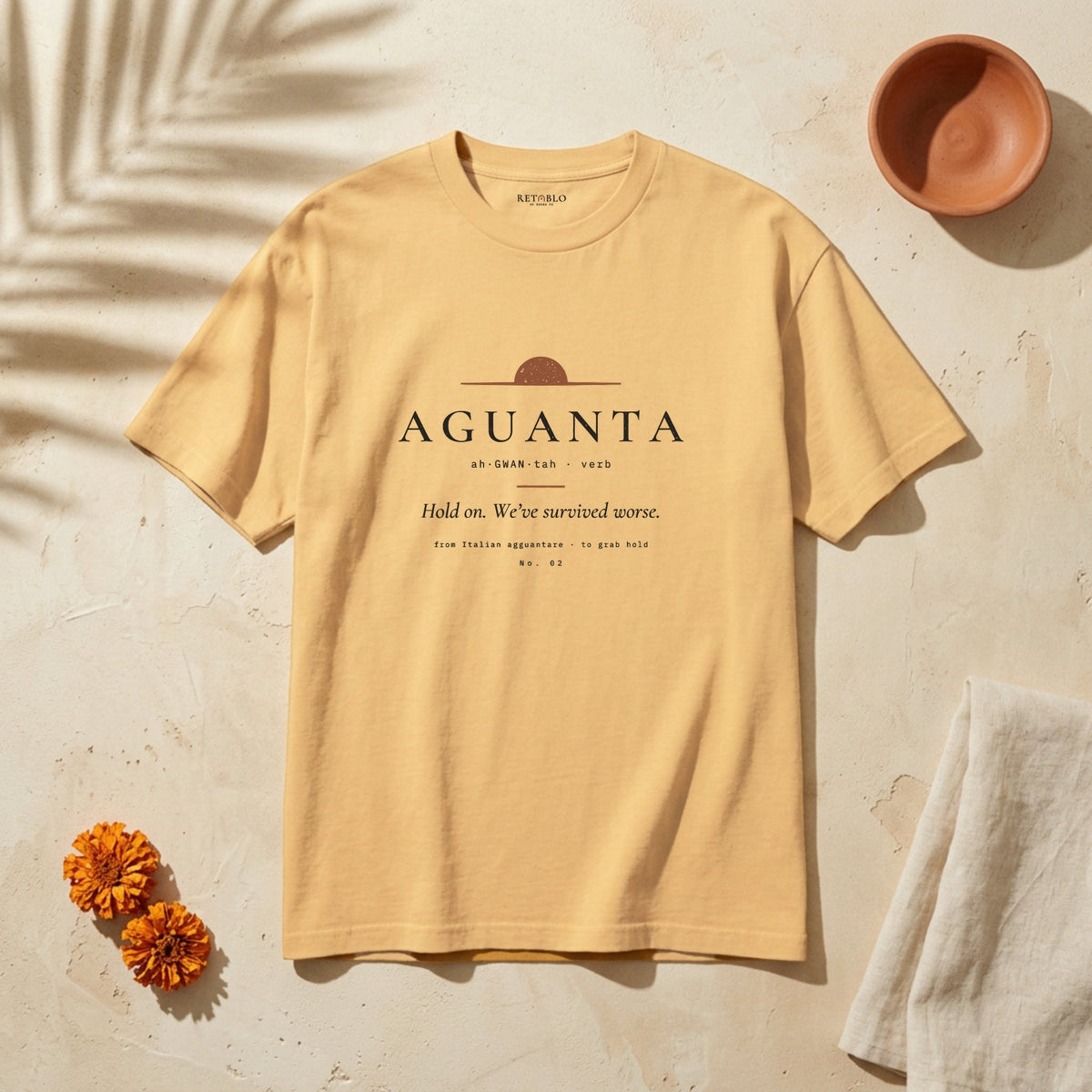 AGUANTA Palabra Tee in Faded Mustard: garment-dyed heavyweight cotton tee printed with a rising dawn sun and the line “Hold on. We’ve survived worse.”