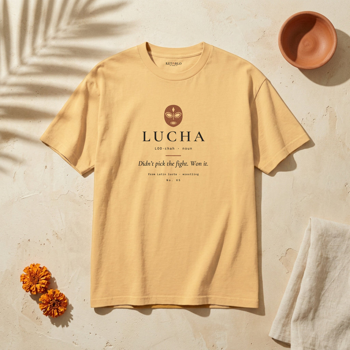 LUCHA Palabra Tee in Faded Mustard: garment-dyed heavyweight cotton tee printed with a luchador mask and the line “Didn’t pick the fight. Won it.”