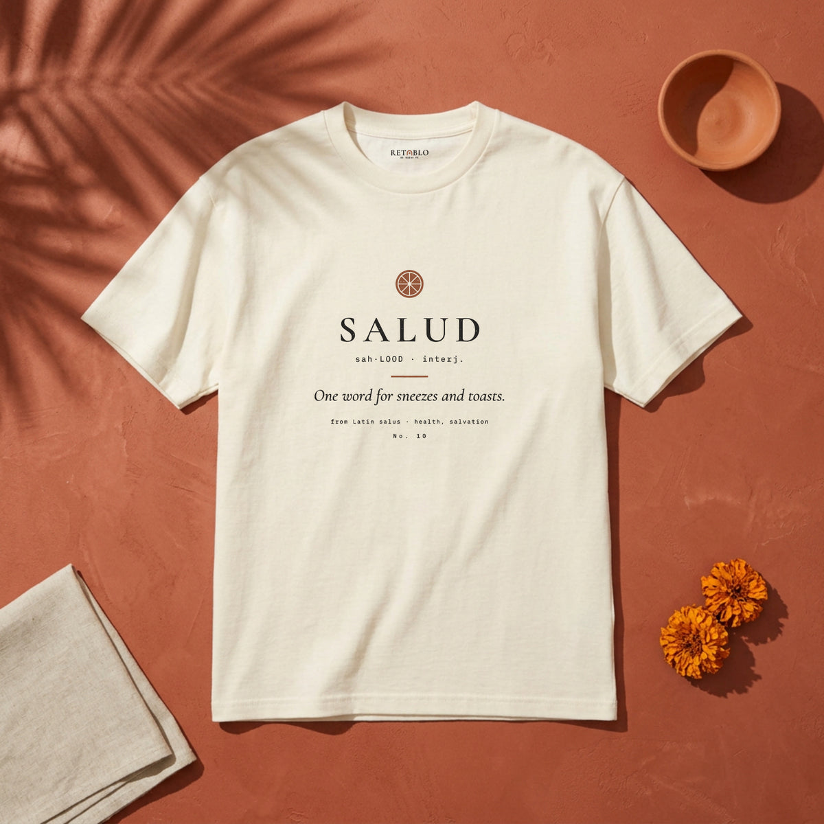 SALUD Palabra Tee in Faded Cream: garment-dyed heavyweight cotton tee printed with a citrus slice and the line “One word for sneezes and toasts.”