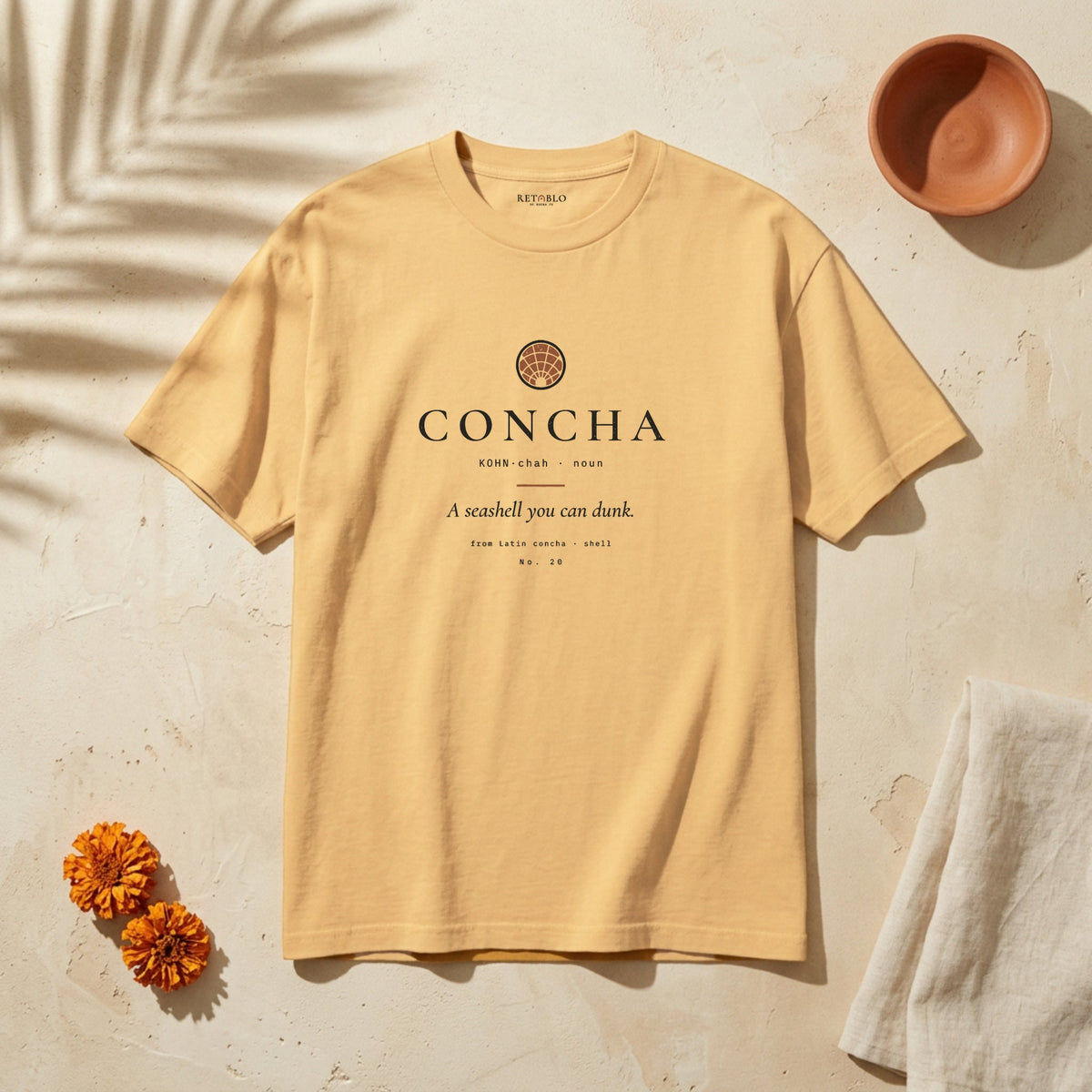 CONCHA Palabra Tee in Faded Mustard: garment-dyed heavyweight cotton tee printed with a concha pastry seen from above and the line “A seashell you can dunk.”