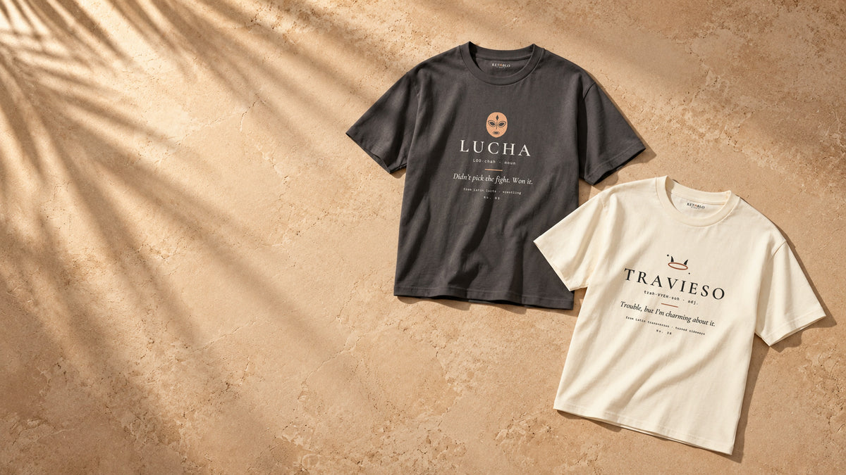 LUCHA Palabra Tee in Faded Black and TRAVIESO Palabra Tee in Faded Cream laid flat on sunlit plaster